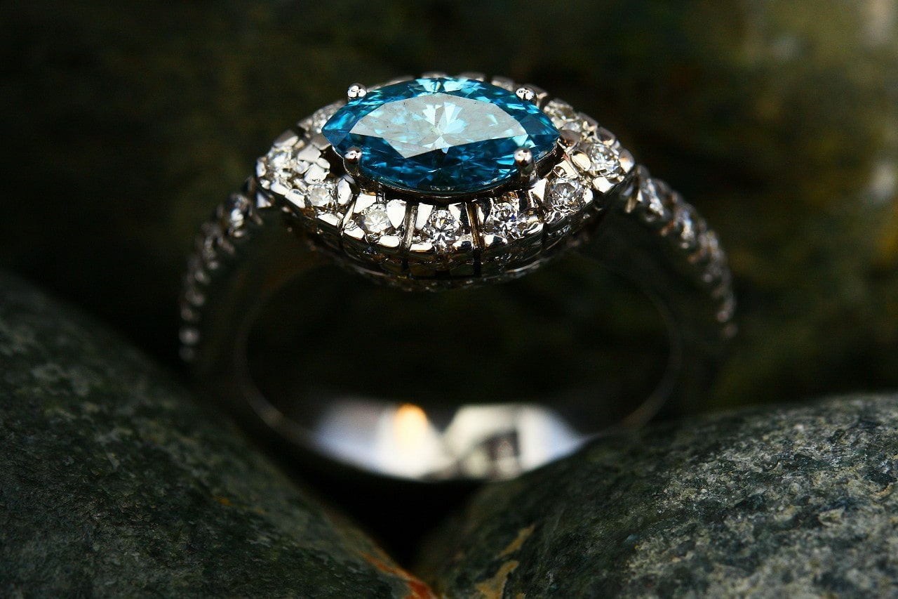 A close-up of a stunning white gold ring featuring a marquise-cut blue gemstone surrounded by small sparkling diamonds, set against a dark, textured background.