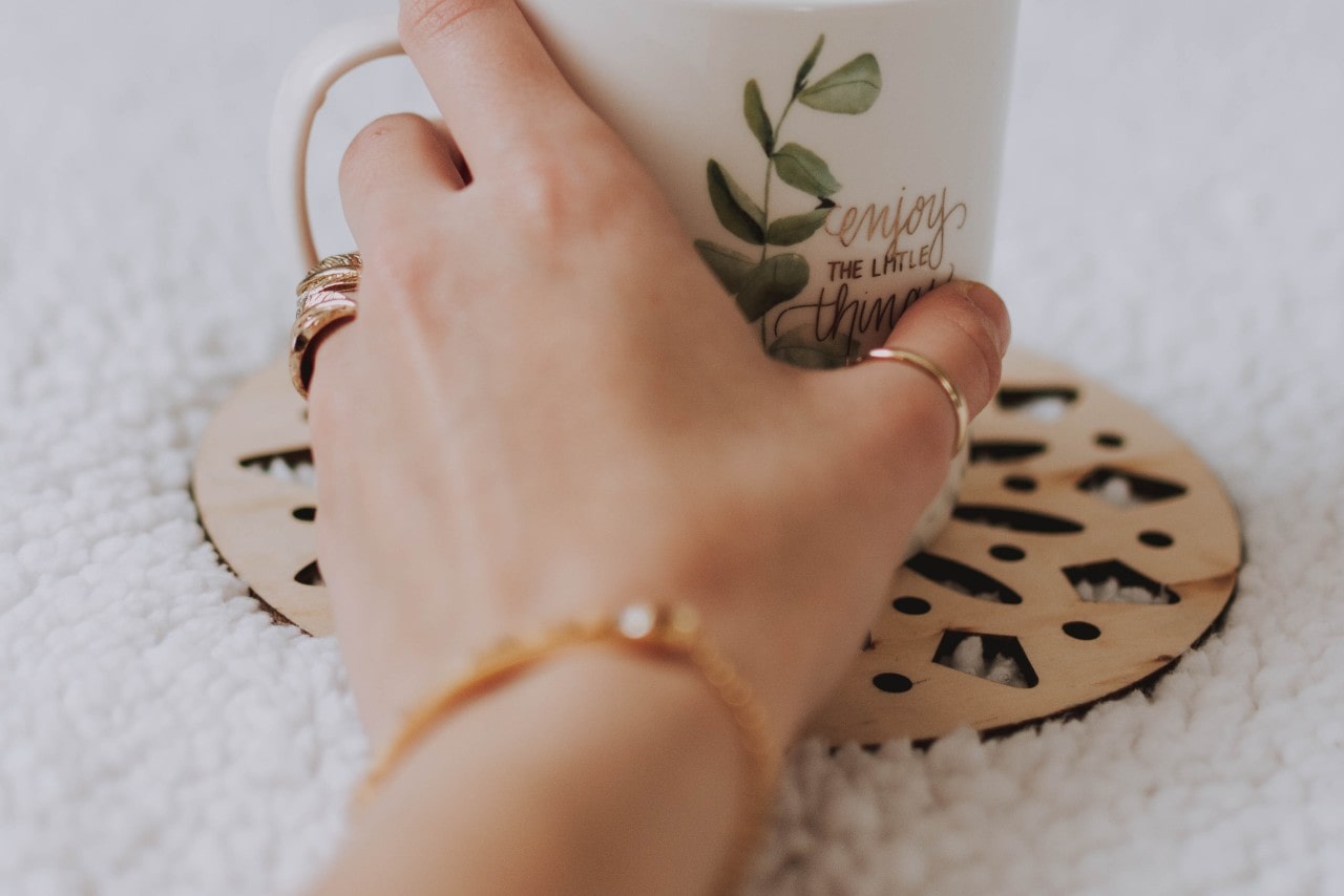 A close-up of a woman’s hand adorned in beautiful gold jewelry, holding a charming mug. A close-up of a woman’s hand adorned in beautiful gold jewelry, holding a charming mug.